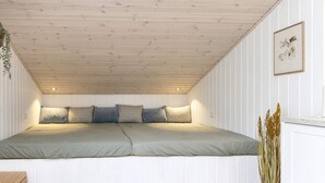 A bedroom with a sloped ceiling, a bed with pillows, a bedside plant, and a framed picture on the wall. - 4 Star Holiday Home in Ansager (Ansager)