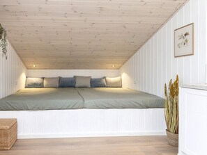 Une chambre avec un plafond en pente, un lit avec des oreillers, une plante sur la table de chevet et un tableau encadré au mur.