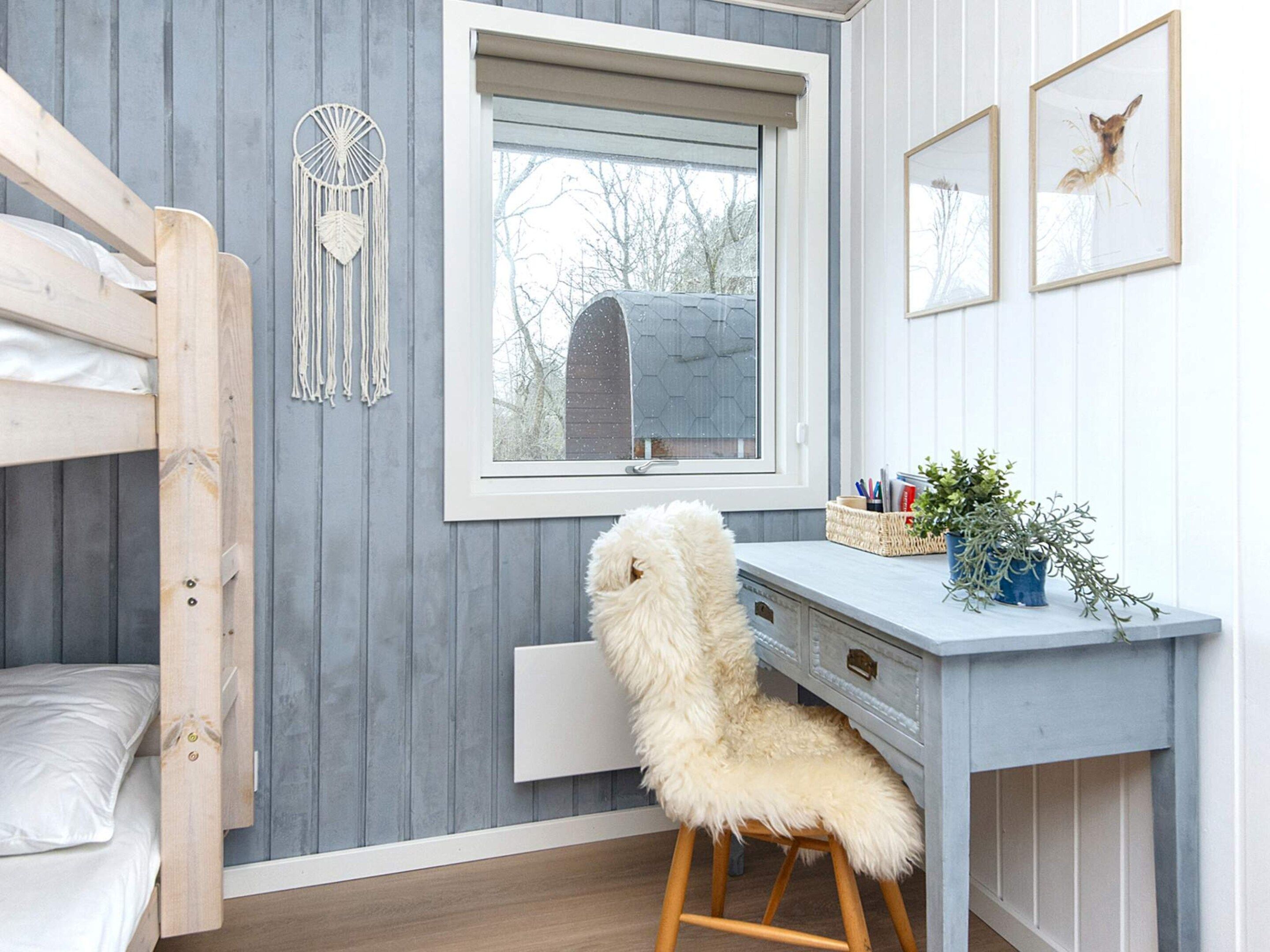 A room with a bunk bed, a desk with a chair, a window with blinds, and wall decorations.