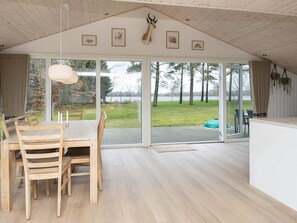 A spacious room with a large dining table, chairs, and a view of a lake through large glass doors. - 4 Star Holiday Home in Ansager (Ansager)