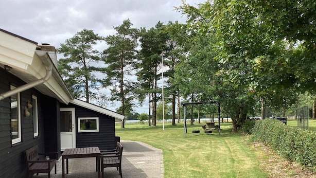 A cabin with a patio, a swing set, and a view of a lake. - 4 Star Holiday Home in Ansager (Ansager)