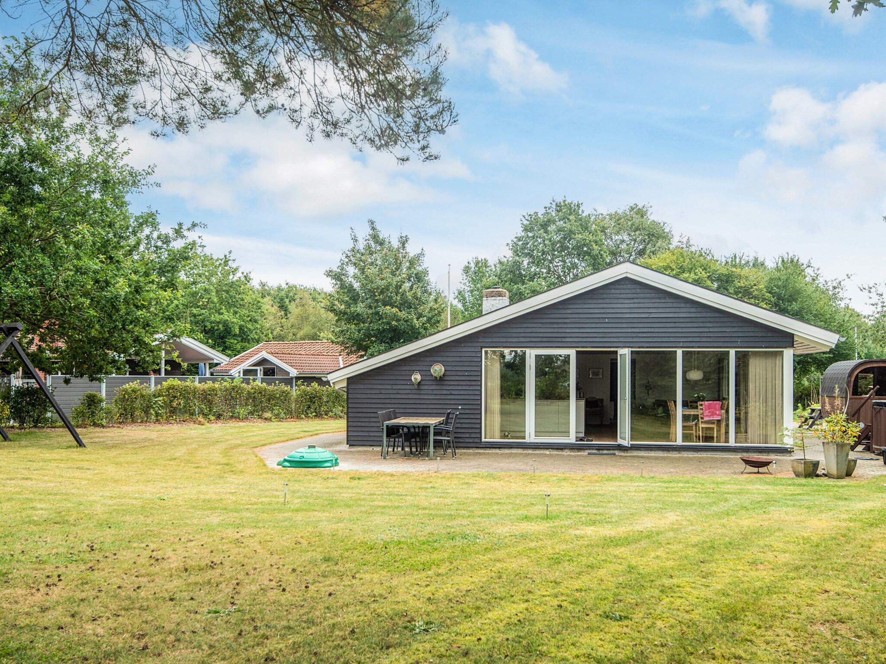 Een gelijkvloers huis met een grote schuifdeur, een klein terras met een tafel en stoelen, en een groen gazon.