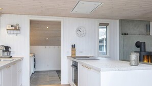 A modern kitchen with white cabinetry, a central island, a built-in oven, and a clock on the wall. - 4 Star Holiday Home in Ansager (Ansager)