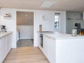 A modern kitchen with white cabinetry, a central island, a built-in oven, and a clock on the wall. - 4 Star Holiday Home in Ansager (Ansager)