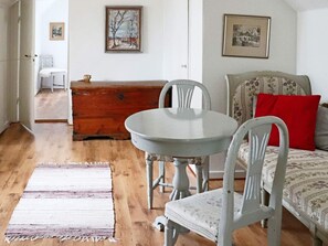 A room with a round table, two chairs, a bed with floral bedding, a red pillow, a wooden dresser, and a rug. - 4 Star Holiday Home in Laholm-by Traum (Laholm)