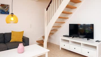 Una sala de estar con un sofá, un televisor sobre un mueble bajo, una escalera y una lámpara colgante.