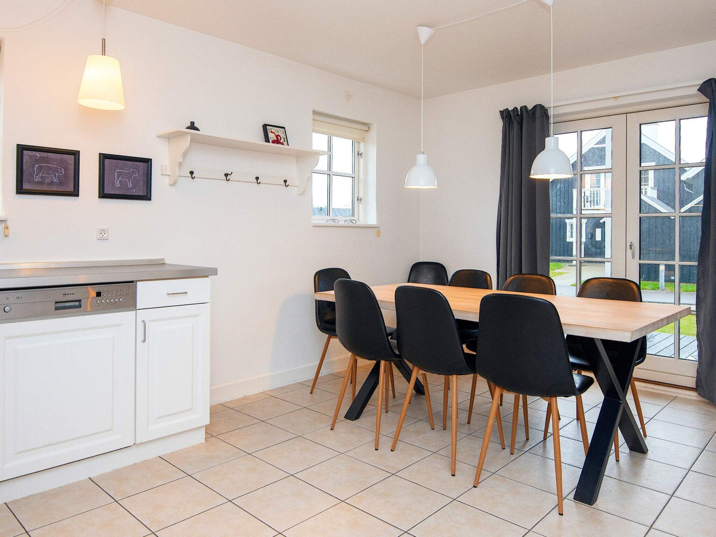 Una cocina moderna con armarios blancos, lavavajillas integrado y comedor con mesa de madera y sillas negras.