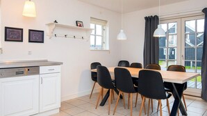Une cuisine moderne avec des meubles blancs, un lave-vaisselle encastré et un coin repas comprenant une table en bois et des chaises noires.