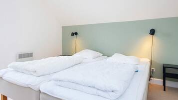 A double bed with white bedding, a wall-mounted lamp, and a bedside table.