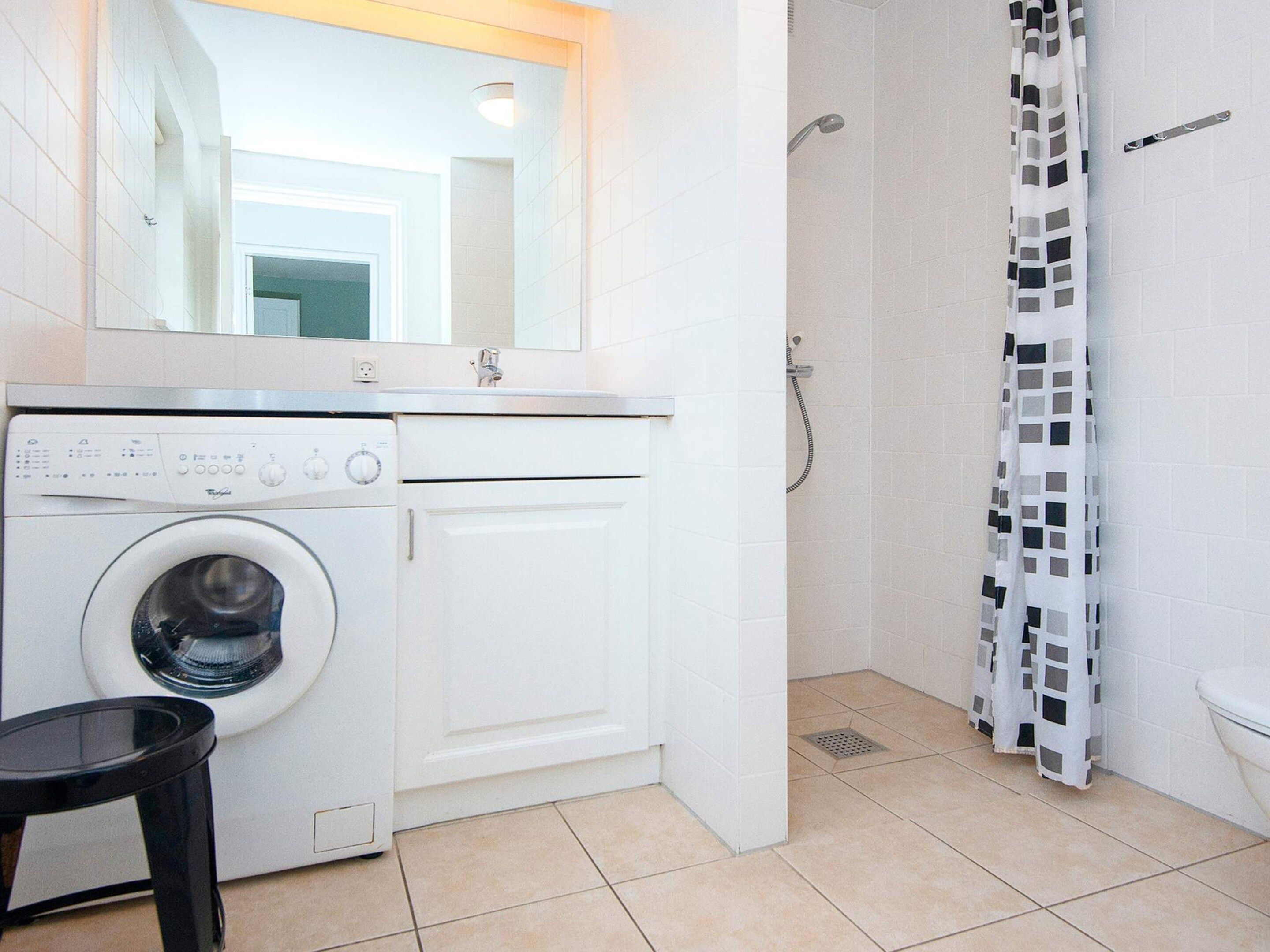 A compact bathroom with a washing machine, a shower, and a toilet.