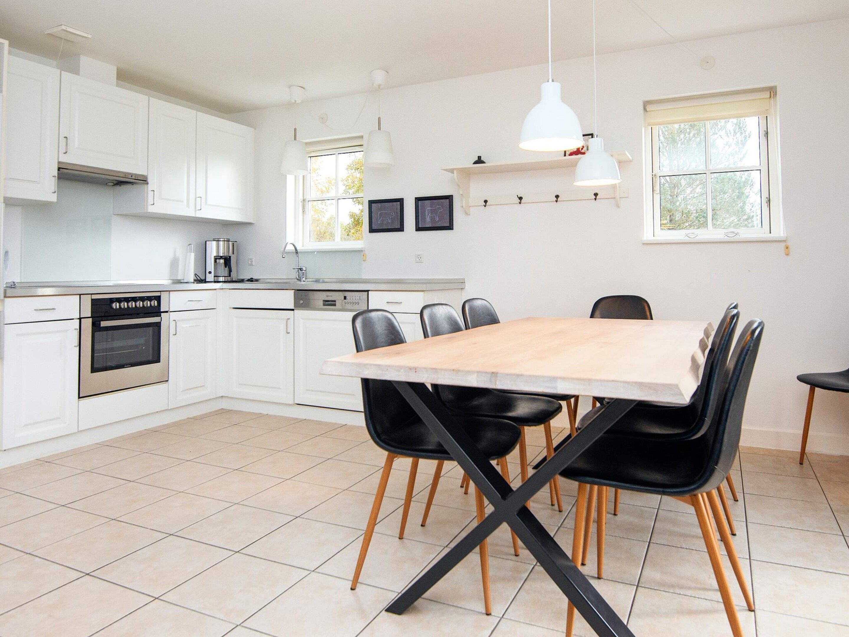 A modern kitchen with white cabinets, a wooden dining table, and black chairs.