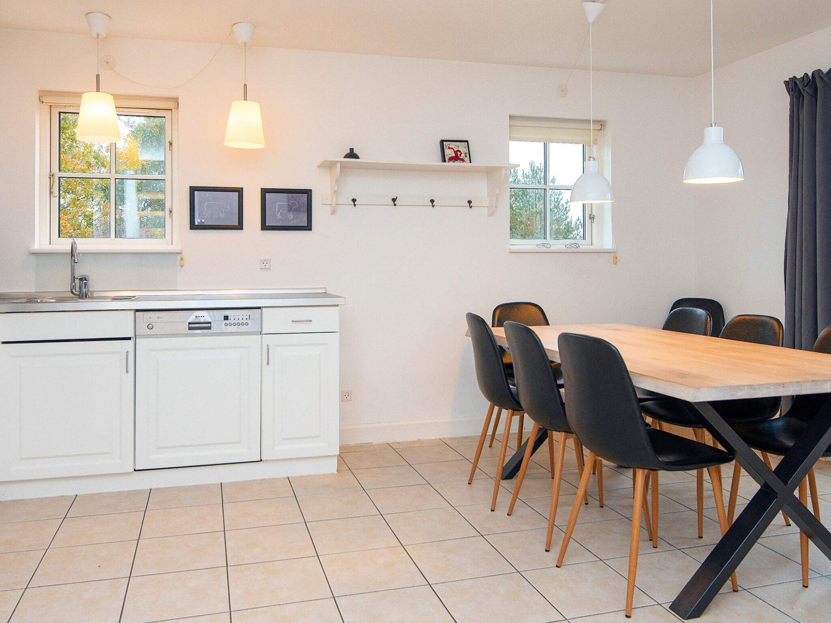 Una cocina moderna con armarios blancos, lavavajillas y un comedor con mesa de madera y sillas negras.
