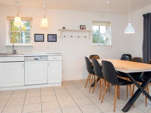 Una cocina moderna con armarios blancos, lavavajillas y un comedor con mesa de madera y sillas negras.