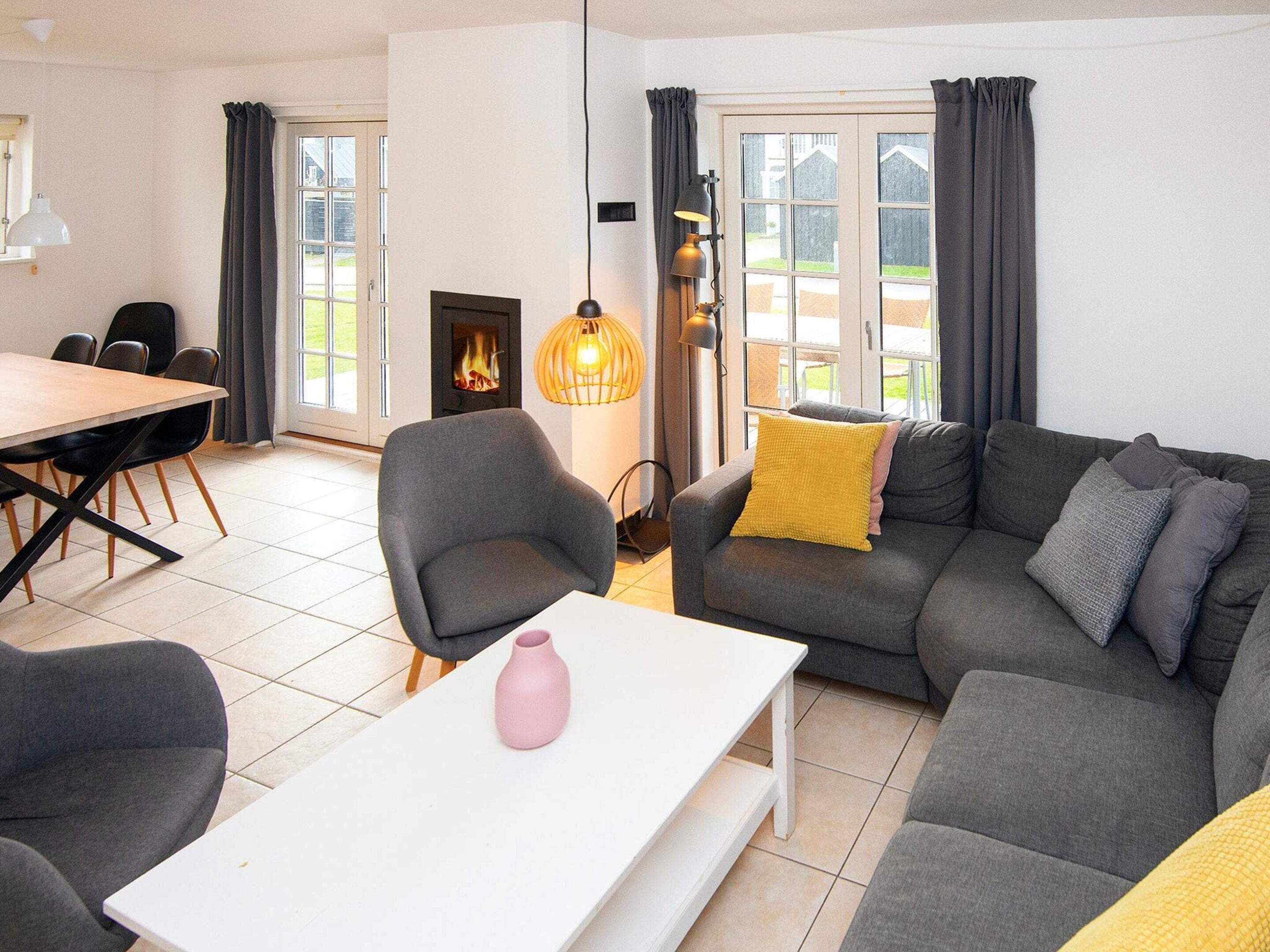 Una sala de estar moderna con un sofá, una mesa de comedor con sillas, una chimenea y vistas amplias por grandes ventanales.