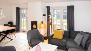 Un salon moderne comprenant un canapé, une table à manger avec des chaises, une cheminée et une vue dégagée grâce à de grandes fenêtres.