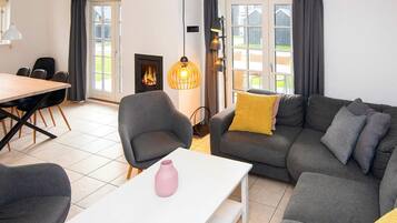 Una sala de estar moderna con un sofá, una mesa de comedor con sillas, una chimenea y vistas amplias por grandes ventanales.