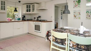 A modern kitchen with white cabinets, a stove, and a dining area with a table covered in a food-themed tablecloth. - 6 Person Holiday Home in Hojby (Hojby)