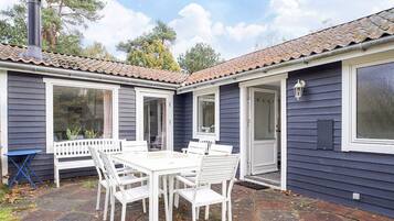 A house with a patio area featuring a white table and chairs, a chimney, and a door leading to the interior.