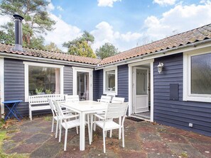 A house with a patio area featuring a white table and chairs, a chimney, and a door leading to the interior.