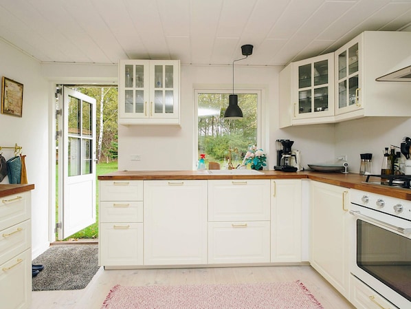 A kitchen with white cabinetry, a wooden countertop, and a window overlooking a garden. - 6 Person Holiday Home in Hojby (Hojby)