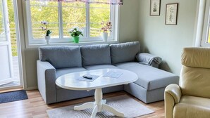 Una sala de estar moderna con un sofá seccional gris, una mesa de centro blanca, un sillón beige y un ventanal con plantas.