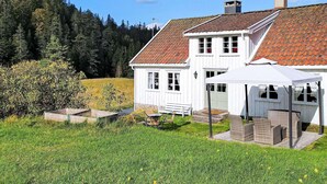 A white house with a red-tiled roof, a covered porch, and a garden with a bench and a table.