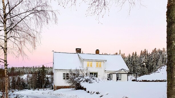 A snow-covered house with a white exterior, a visible chimney, and a small porch area.
