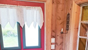 A wooden door with a red panel, lace trim, and a window with a white curtain.