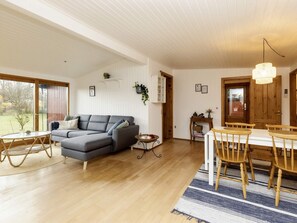 A spacious living room with a grey sofa, wooden dining table, and chairs. There is a small side table and a hanging light fixture. - 4 Person Holiday Home in Vaeggerlose (Vaeggerlose)