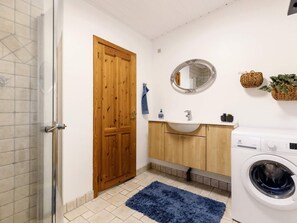 A compact bathroom with a wooden door, a round mirror, a sink, a washing machine, and a blue rug. - 4 Person Holiday Home in Vaeggerlose (Vaeggerlose)