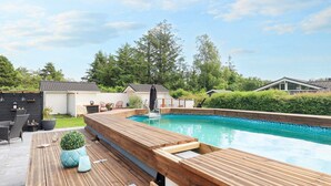 A swimming pool with a wooden deck, surrounded by greenery and a clear sky. - 5 Star Holiday Home in Hals (Hals)