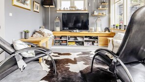 A modern living room with a flat-screen TV, leather chairs, a cowhide rug, and a wooden entertainment unit. - 5 Star Holiday Home in Hals (Hals)
