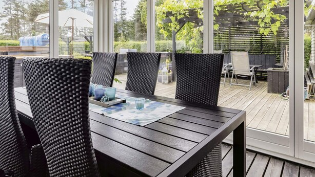 A covered patio with a table and chairs, large windows, and a view of greenery. - 5 Star Holiday Home in Hals (Hals)