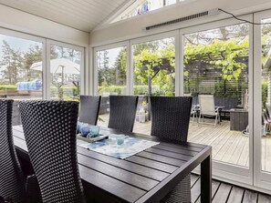 A covered patio with a table and chairs, large windows, and a view of greenery. - 5 Star Holiday Home in Hals (Hals)