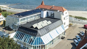 A modern hotel with a glass facade, a red-roofed building, and a view of the sea. - 4 Star Holiday Home in Hejls (Hejls)