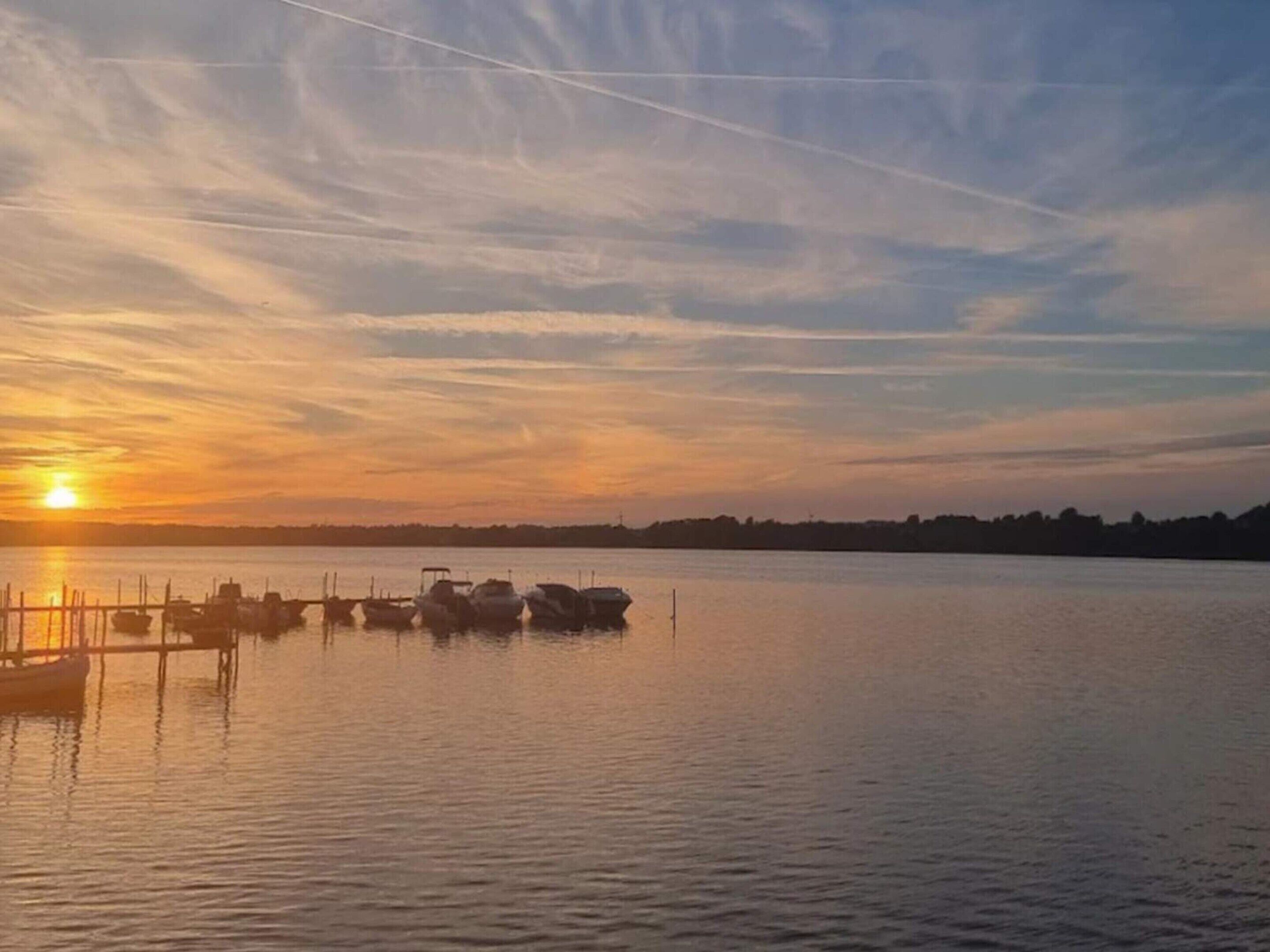 Ruhige Wasserfläche mit Booten, die an einem Steg liegen, bei Sonnenuntergang.