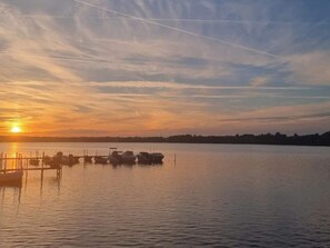 A calm body of water with boats docked at a pier during sunset.