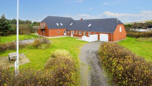 A large brick building with a sloped roof, a white garage door, and a grassy yard with a gravel path. - 4 Star Holiday Home in Ulfborg (Ulfborg)