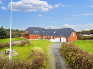 A large brick building with a sloped roof, a white garage door, and a grassy yard with a gravel path. - 4 Star Holiday Home in Ulfborg (Ulfborg)