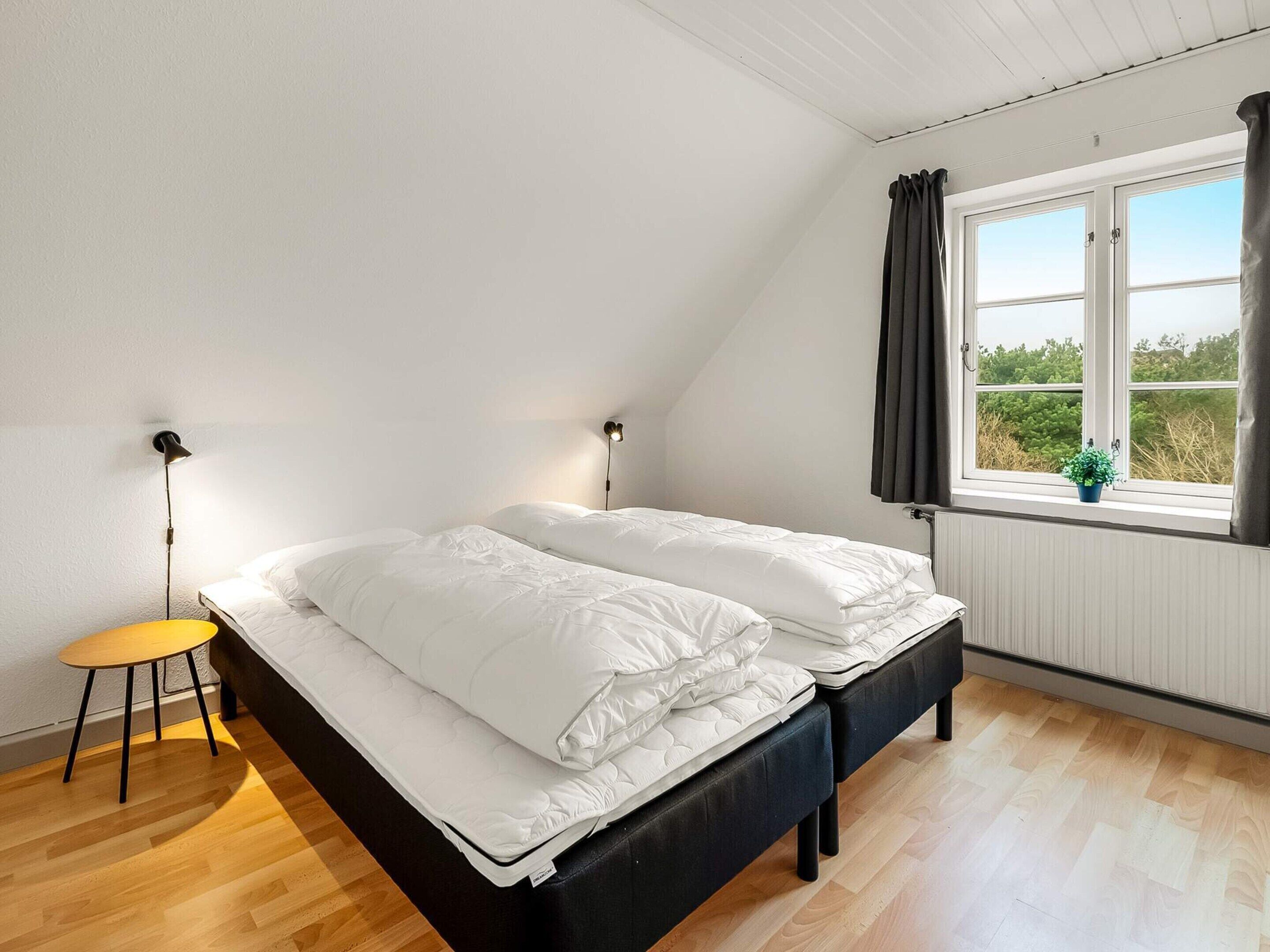 A bedroom with a bed, bedside lamps, a small table, and a window with curtains.