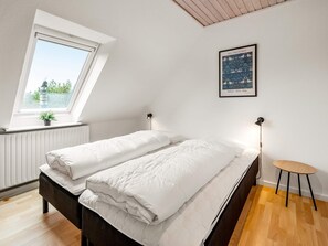 Et soveværelse med seng, et vindue, en radiator, en vægmonteret lampe og et indrammet billede.