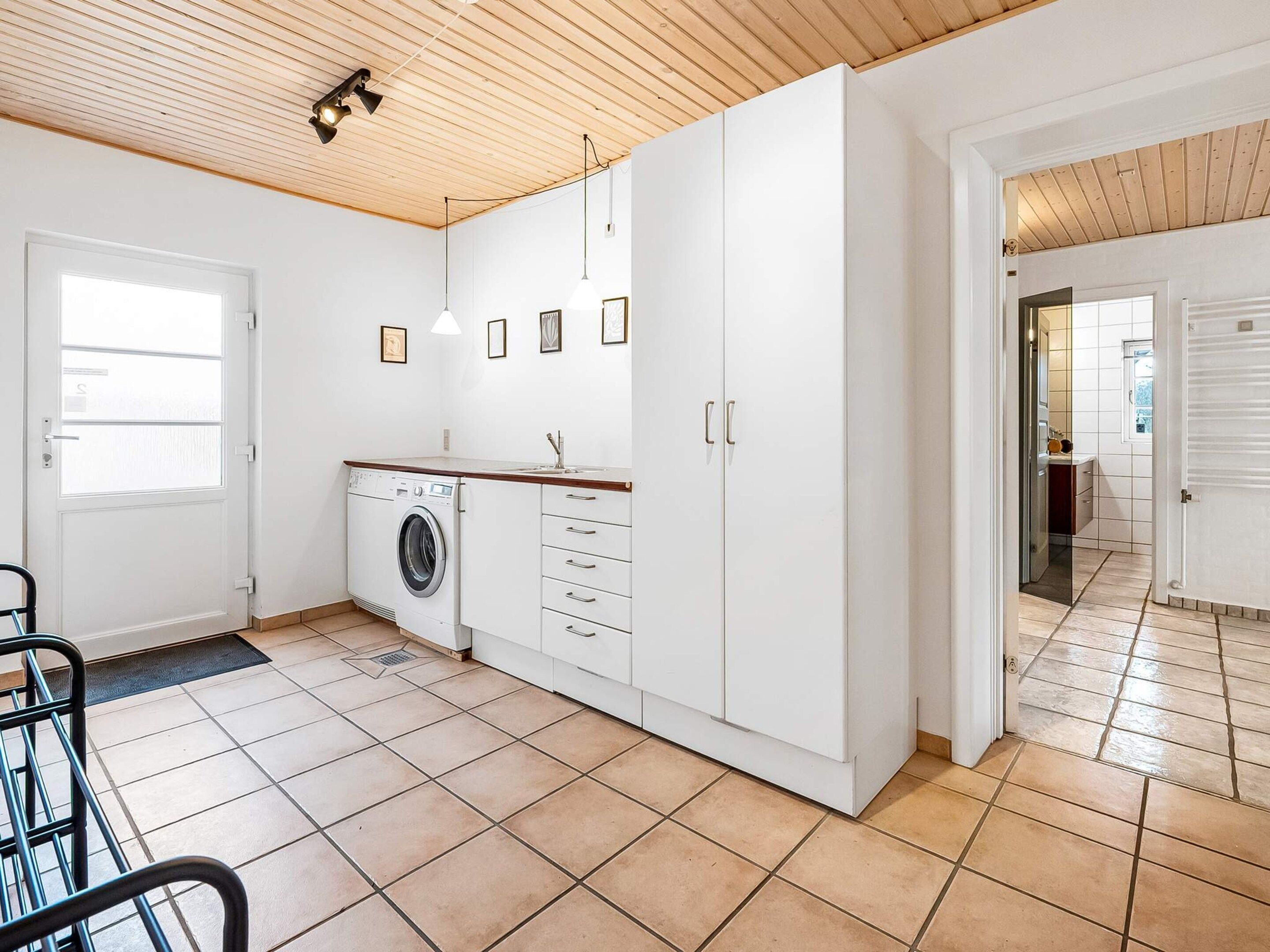 Ett modernt kök med tvättmaskin, vita skåp och ett träpanelat tak.