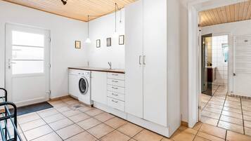 A modern kitchen with a washing machine, white cabinets, and a wooden ceiling.