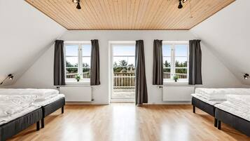 Ein Schlafzimmer mit zwei Betten, Holzboden, einer schrägen Decke mit Leuchten und großen Fenstern mit Vorhängen.