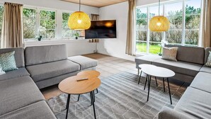 Un salon moderne doté d’un téléviseur à écran plat, de deux canapés, d’une table basse et de grandes fenêtres avec des rideaux.