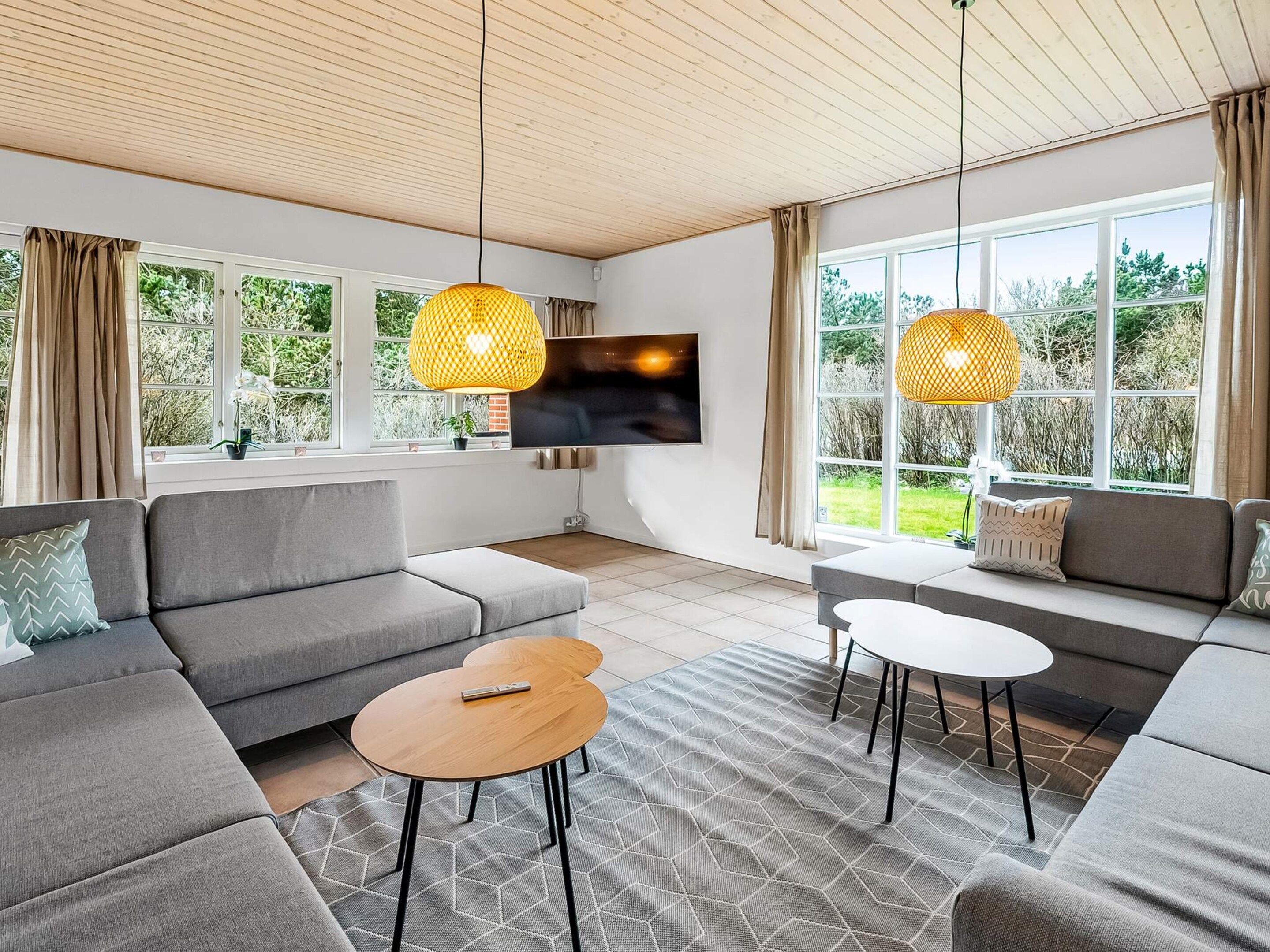 A modern living room with a sectional sofa, a flat-screen TV, and two pendant lights.
