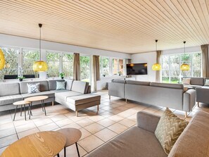 En moderne stue med en hjørnesofa, et sofabord og et fjernsyn monteret på væggen.