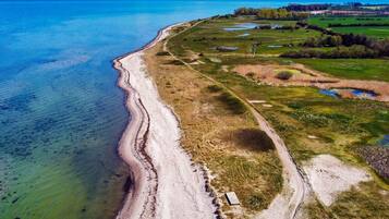 An aerial view of a coastal area with a beach, a dirt path, and green fields.