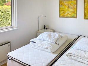 Een eenpersoonsbed met een gebogen matras, een nachtkastje met een lamp, en twee abstracte schilderijen aan de muur.