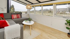 A modern living room with a grey sofa, a small white table, and a large window offering a view of the outdoors. - 6 Person Holiday Home in Olsted (Frederiksvaerk)